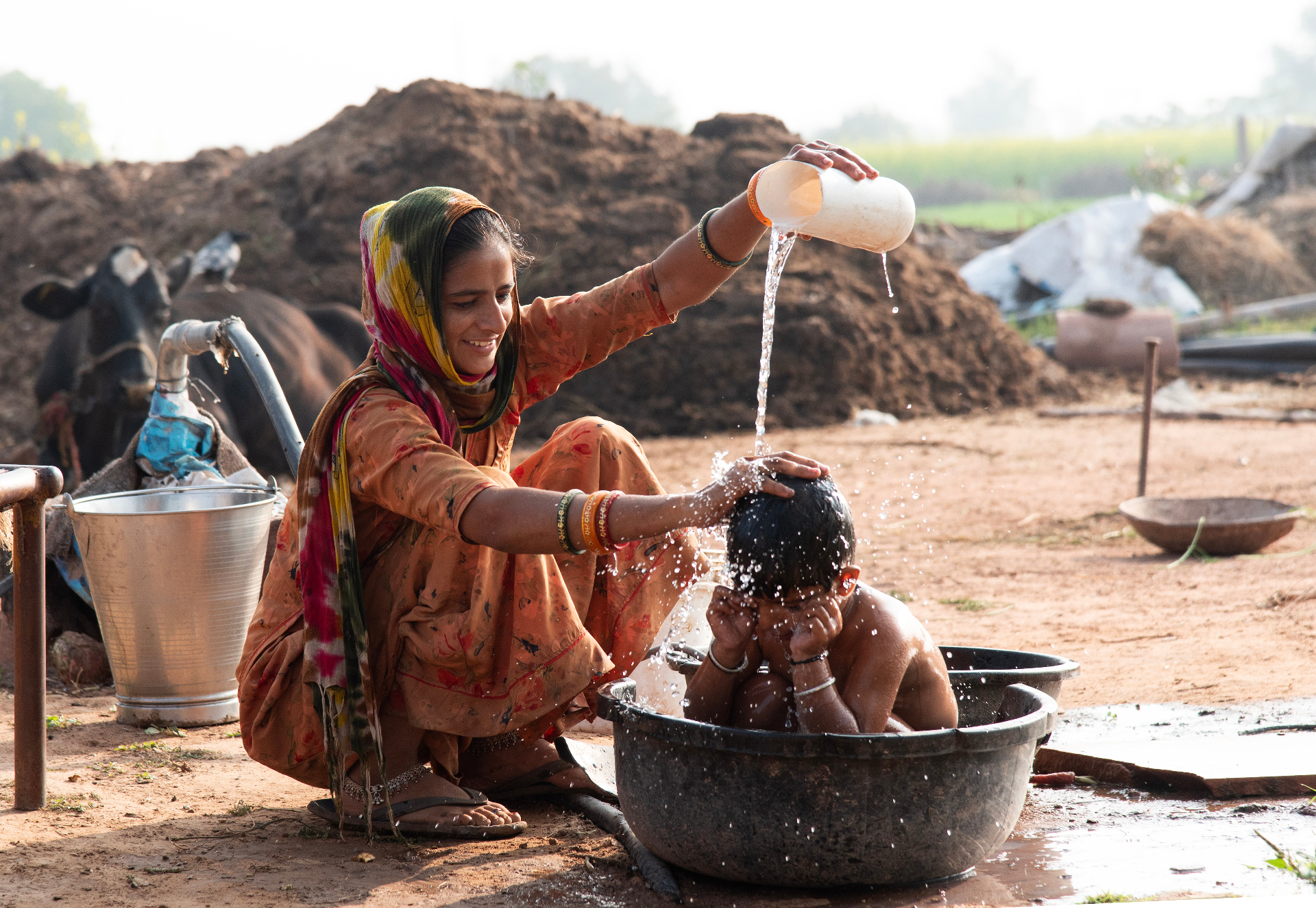 A woman bathing a child outdoors at a village water source